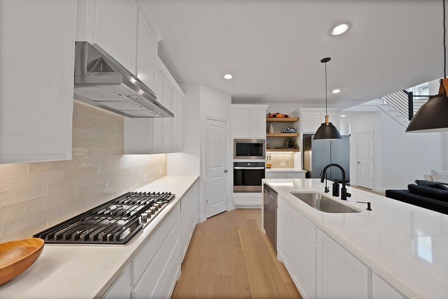 Modern kitchen featuring light wood-finish flooring, white cabinetry, integrated stainless steel appliances, and an expansive island with an undermount sink and matte black fixtures