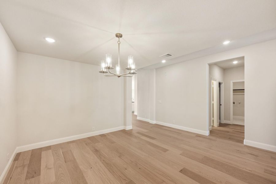 Empty room with light hardwood floors, white walls, and a modern chandelier with glass shades Empty room with light hardwood floors, white walls, and a modern chandelier with glass shades