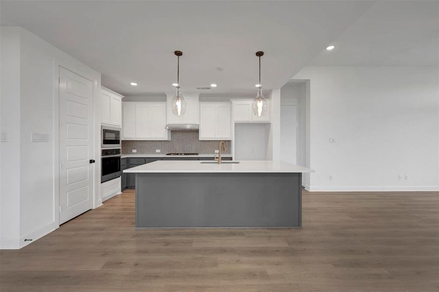 The kitchen features a large island with a light-colored countertop, white upper cabinetry, grey base cabinetry, and a tile backsplash