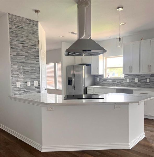 Kitchen with decorative light fixtures, tasteful backsplash, stainless steel fridge, and island range hood