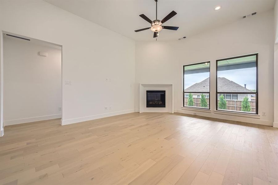 Unfurnished living room with light wood-type flooring, baseboards, a glass covered fireplace, a ceiling fan, and recessed lighting