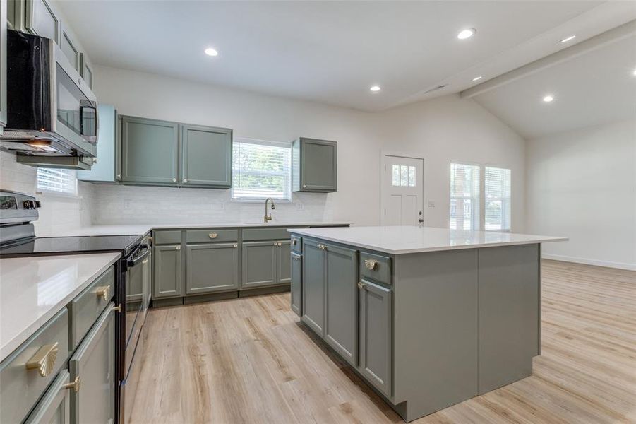 Kitchen featuring lofted ceiling with beams, stainless steel appliances, light hardwood / wood-style floors, a kitchen island, and decorative backsplash