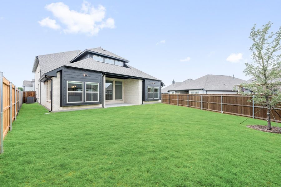 Backyard of a home with dark exterior, covered patio, large green lawn, and wood privacy fence. Backyard of a home with dark exterior, covered patio, large green lawn, and wood privacy fence.