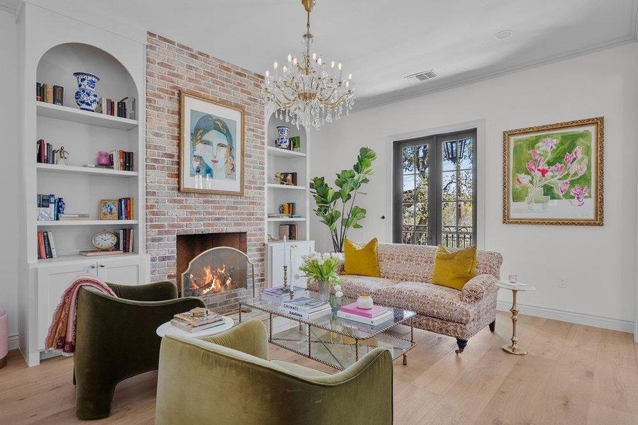 Living room featuring light wood-style flooring, hanging lights, a fireplace, ornamental molding, and built in features