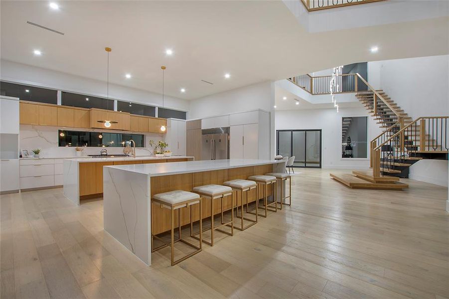 Kitchen with white cabinets, light wood-type flooring, a large island, and stainless steel built in refrigerator