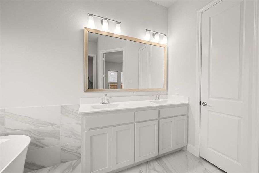 Full bath featuring double vanity, a freestanding bath, and marble finish floors