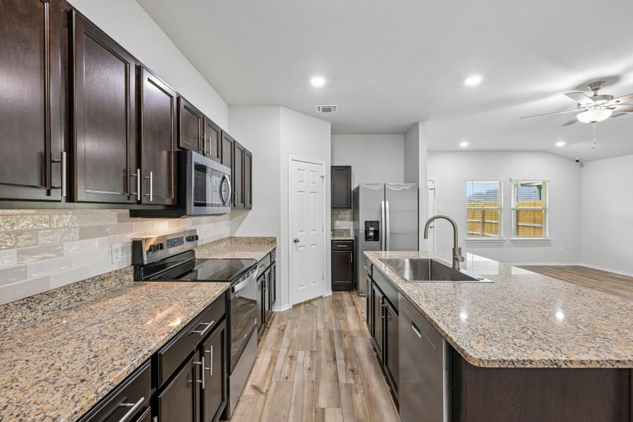 Modern kitchen featuring dark wood cabinetry, granite countertops, stainless steel appliances, a tile backsplash, and wood-finish flooring