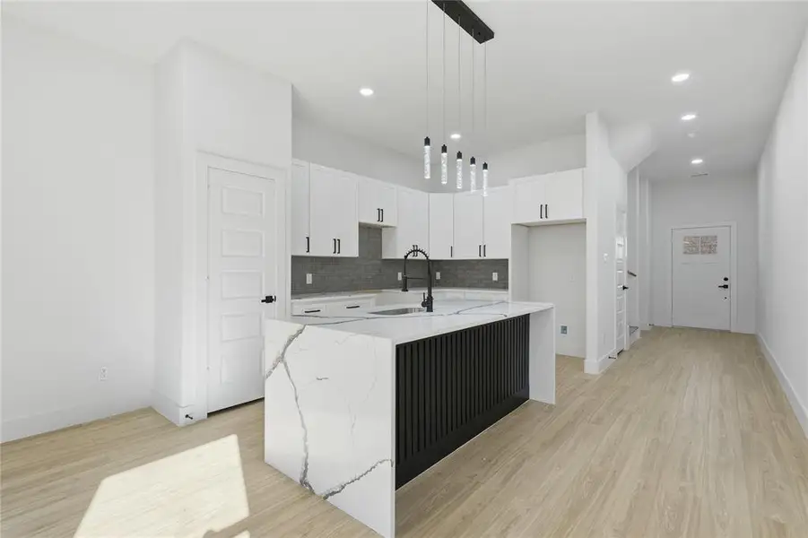 Kitchen featuring light stone counters, a kitchen island with sink, white cabinets, and light wood-style flooring Kitchen featuring light stone counters, a kitchen island with sink, white cabinets, and light wood-style flooring