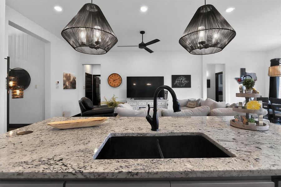 Kitchen island featuring a dual-basin undermount sink with a matte black gooseneck faucet, light-toned speckled countertop, and two ornate black pendant lights