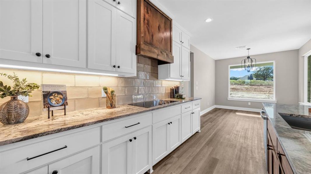 Kitchen with light hardwood / wood-style flooring, white cabinets, black electric stovetop, and light stone countertops