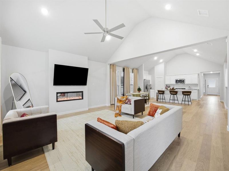 Living room featuring high vaulted ceiling, light wood-type flooring, a glass covered fireplace, recessed lighting, and a ceiling fan