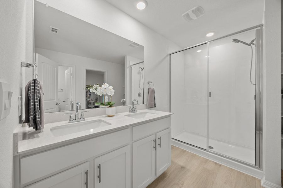 Bathroom with double vanity, a stall shower, and light wood-type flooring