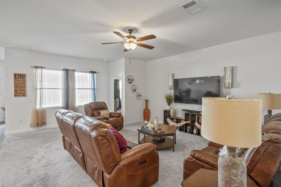 Carpeted living room featuring a ceiling fan and baseboards