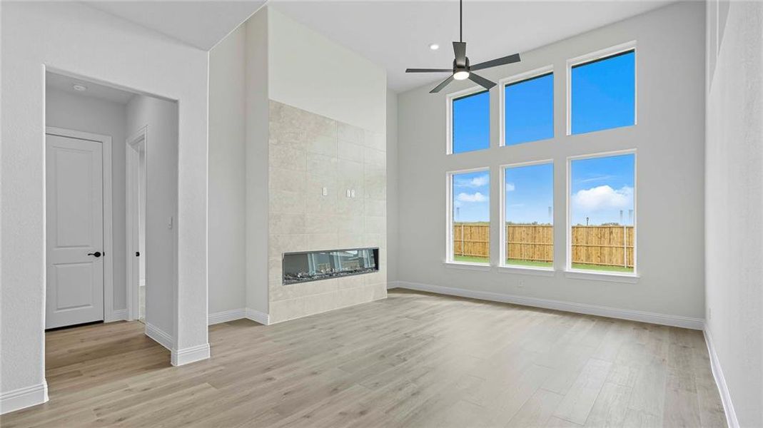 Spacious living area featuring a tall ceiling, a linear fireplace with a light-toned tile surround, and a ceiling fan