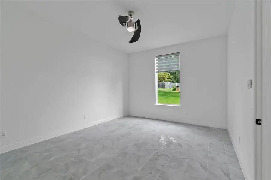 Spacious room featuring large format grey tile flooring, white walls, a single window with horizontal blinds, and a contemporary ceiling fan with integrated lighting