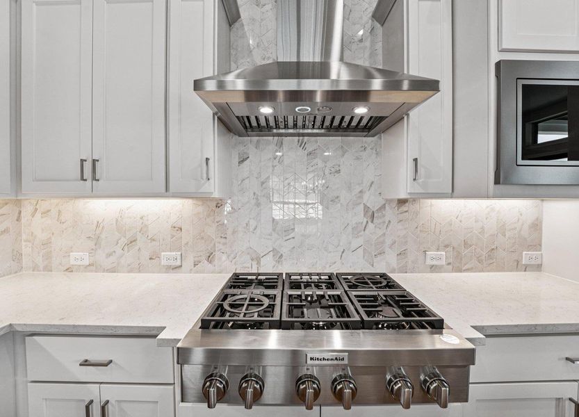 Kitchen featuring wall chimney range hood, stainless steel gas stovetop, light stone countertops, decorative backsplash, and white cabinets
