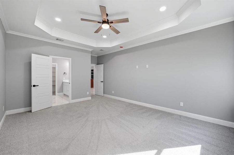 Unfurnished bedroom featuring a tray ceiling, light carpet, crown molding, a ceiling fan, and ensuite bathroom Unfurnished bedroom featuring a tray ceiling, light carpet, crown molding, a ceiling fan, and ensuite bathroom