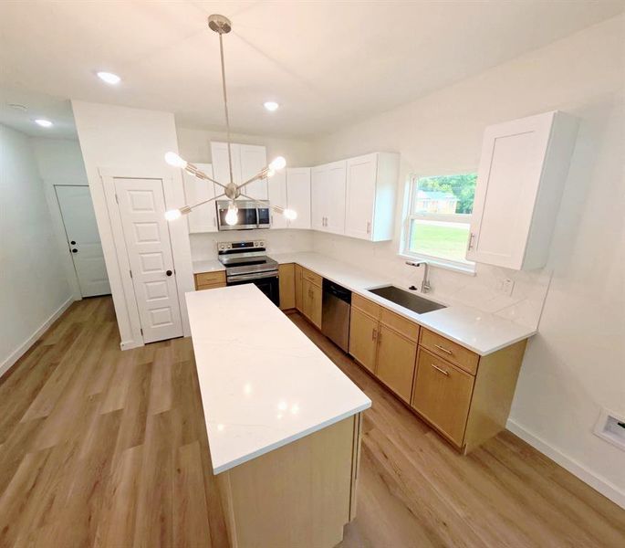 Kitchen with appliances with stainless steel finishes, a chandelier, a center island, light wood-style flooring, and recessed lighting Kitchen with appliances with stainless steel finishes, a chandelier, a center island, light wood-style flooring, and recessed lighting