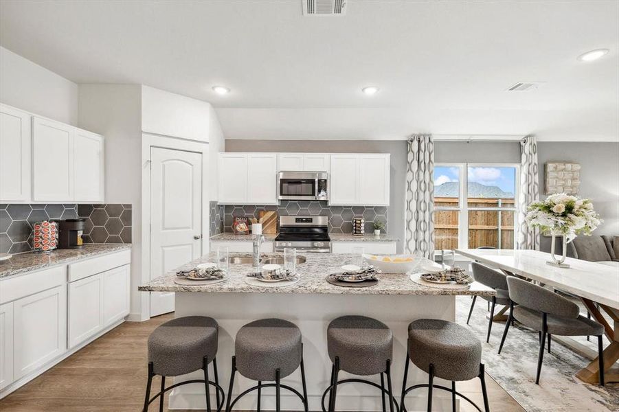 Kitchen featuring light stone countertops, white cabinetry, appliances with stainless steel finishes, light wood finished floors, and decorative backsplash