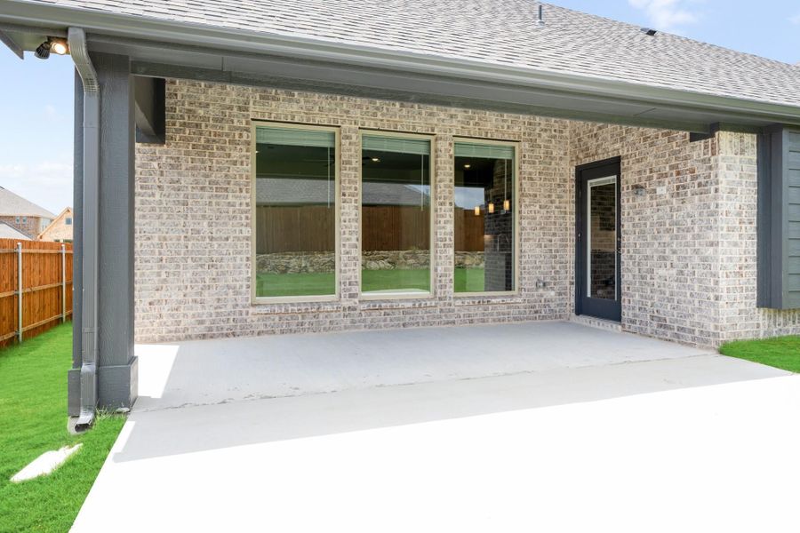 Covered back patio with concrete slab, brick exterior, large windows, and dark door leading inside Covered back patio with concrete slab, brick exterior, large windows, and dark door leading inside