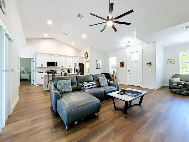 Open floor plan featuring vaulted ceilings, wood-finish flooring, recessed lighting, and a kitchen with white cabinetry and a center island