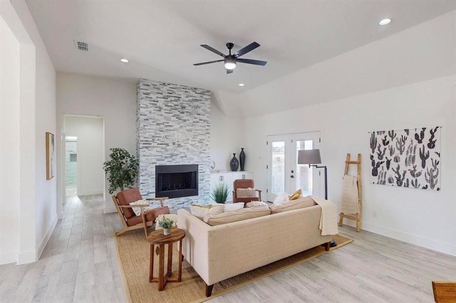 Living room featuring french doors, vaulted ceiling, ceiling fan, light hardwood / wood-style flooring, and a stone fireplace