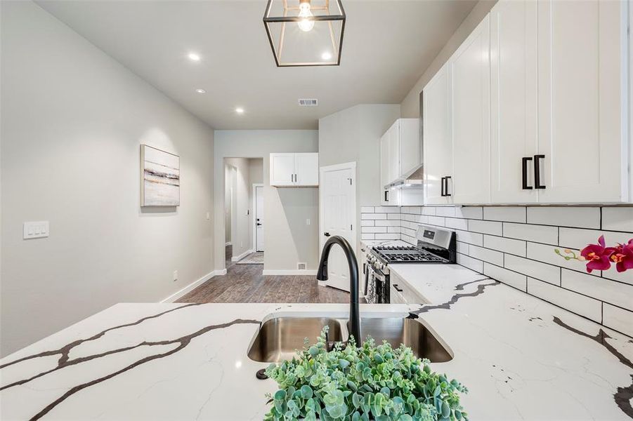 Kitchen featuring light stone counters, stainless steel gas stove, white cabinets, backsplash, and wood finished floors