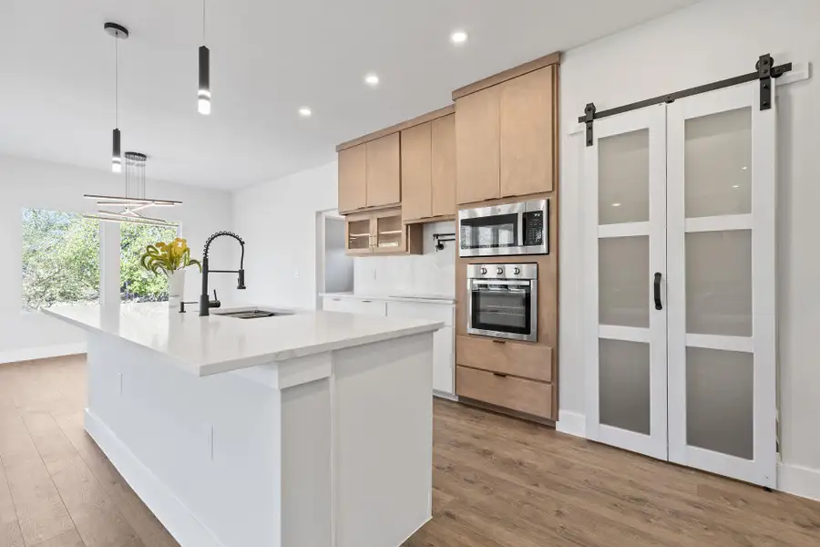 Kitchen featuring pendant lighting, a barn door, stainless steel appliances, an island with sink, and recessed lighting