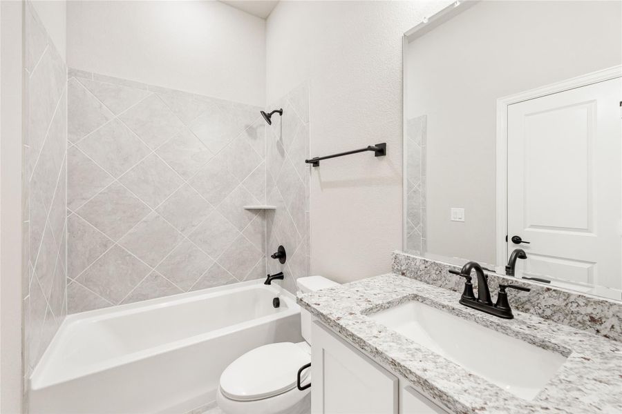 Full bathroom with tub-shower combo, diagonal tile surround, granite vanity, and black fixtures