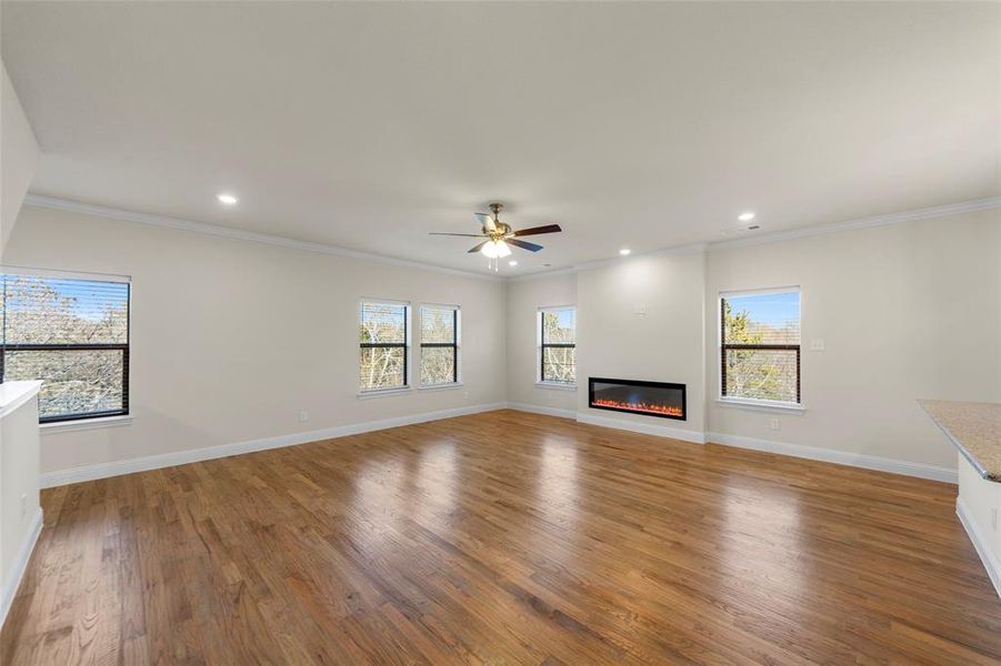 Unfurnished living room featuring a ceiling fan, light wood-style floors, a glass covered fireplace, recessed lighting, and crown molding