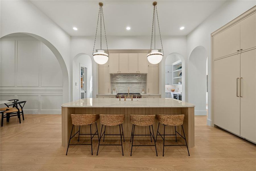 Spacious kitchen featuring a large central island with seating, pendant lighting, light-toned cabinetry, and wood-finish flooring