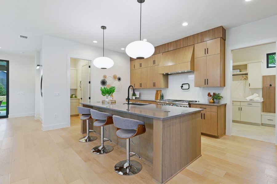 Kitchen featuring premium range hood, light wood finished floors, recessed lighting, decorative backsplash, and a breakfast bar area