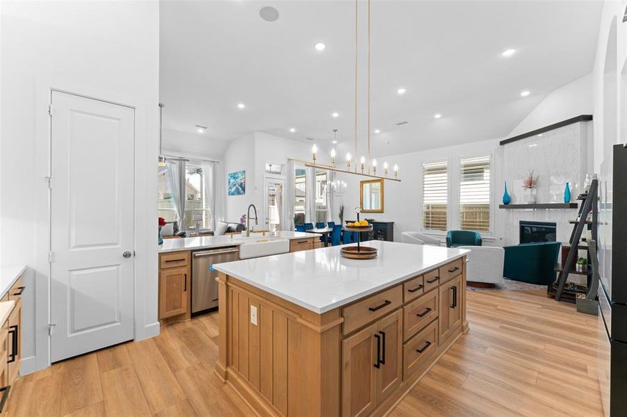 Kitchen featuring open floor plan, decorative light fixtures, a tile fireplace, a kitchen island, and brown cabinets Kitchen featuring open floor plan, decorative light fixtures, a tile fireplace, a kitchen island, and brown cabinets