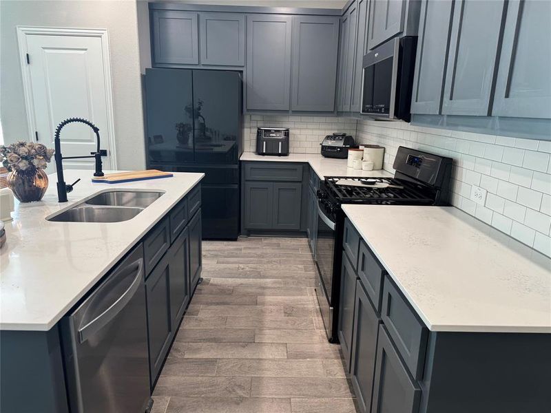 Kitchen with black appliances, decorative backsplash, light stone countertops, and light wood-style flooring Kitchen with black appliances, decorative backsplash, light stone countertops, and light wood-style flooring