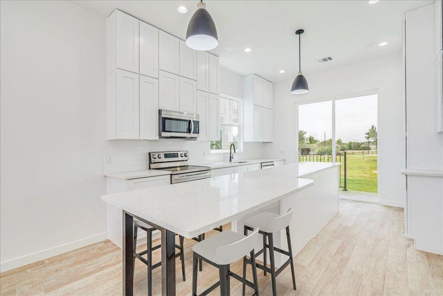 Open kitchen with eat in quartz countertop and stainless steel appliances.