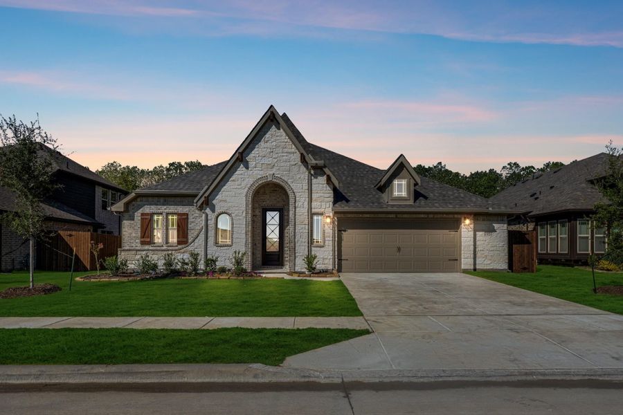 Single-story home with white stone exterior, arched entry, two-car garage, and green front lawn at dusk.