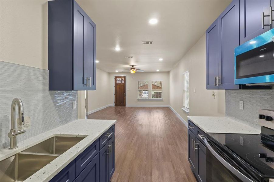 Kitchen with electric stove, blue cabinets, light hardwood / wood-style floors, and sink