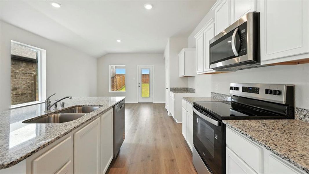 Modern kitchen featuring white cabinetry, granite countertops, and stainless steel appliances including a microwave, dishwasher, and electric range Modern kitchen featuring white cabinetry, granite countertops, and stainless steel appliances including a microwave, dishwasher, and electric range