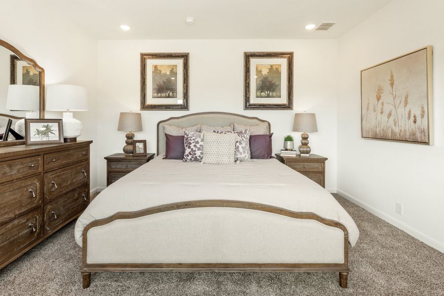 Bedroom with upholstered wood-frame bed, dark wood dresser, nightstands, and carpet flooring