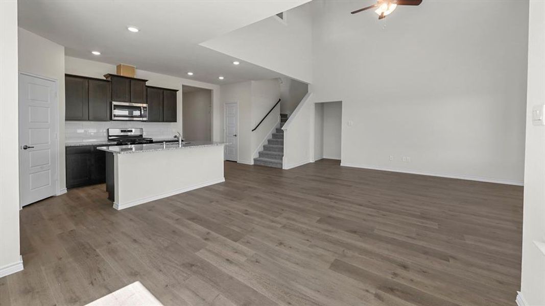Kitchen with a center island with sink, light stone countertops, appliances with stainless steel finishes, open floor plan, and light wood finished floors