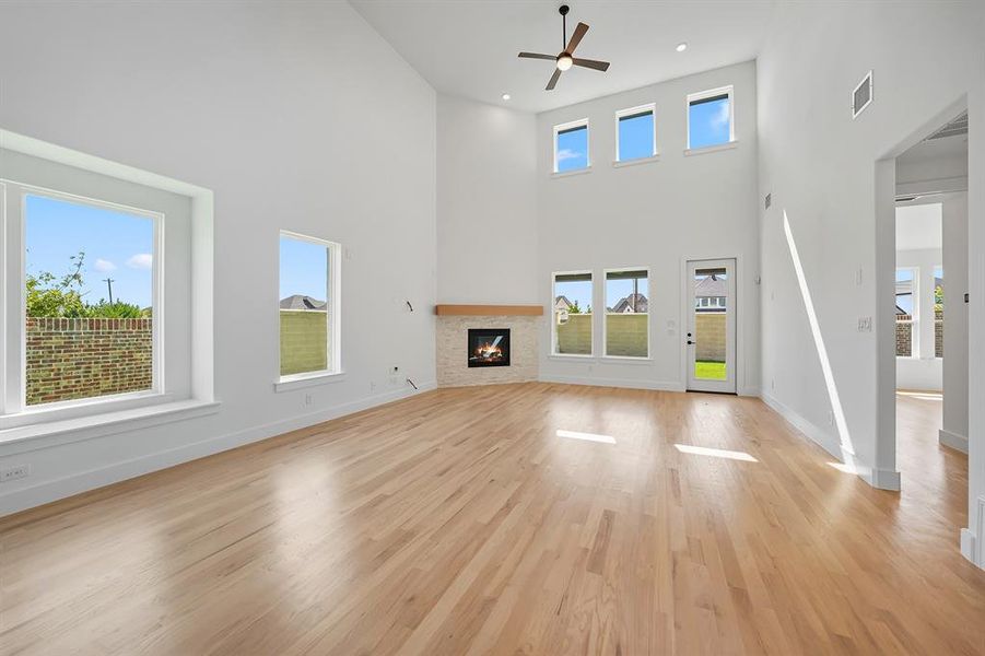 Unfurnished living room with a high ceiling, a glass covered fireplace, light wood-style floors, ceiling fan, and recessed lighting