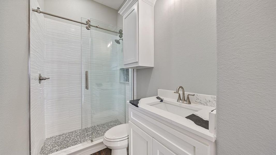 Bathroom with a textured wall, vanity, a shower stall, and toilet