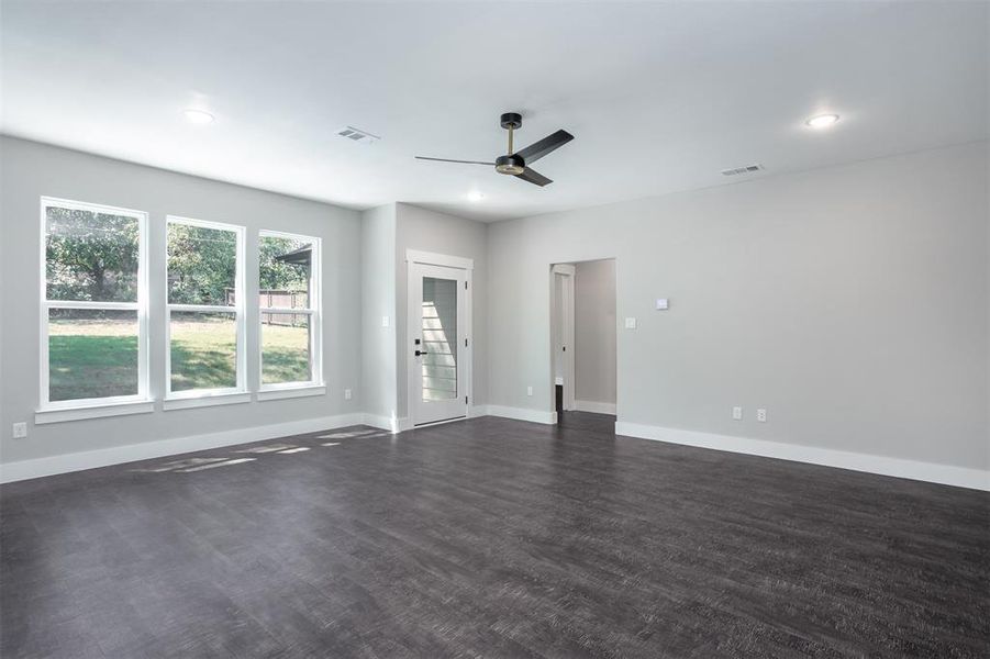 Living room featuring dark wood floors, ceiling fan, large windows to back yard, and recessed lighting Living room featuring dark wood floors, ceiling fan, large windows to back yard, and recessed lighting
