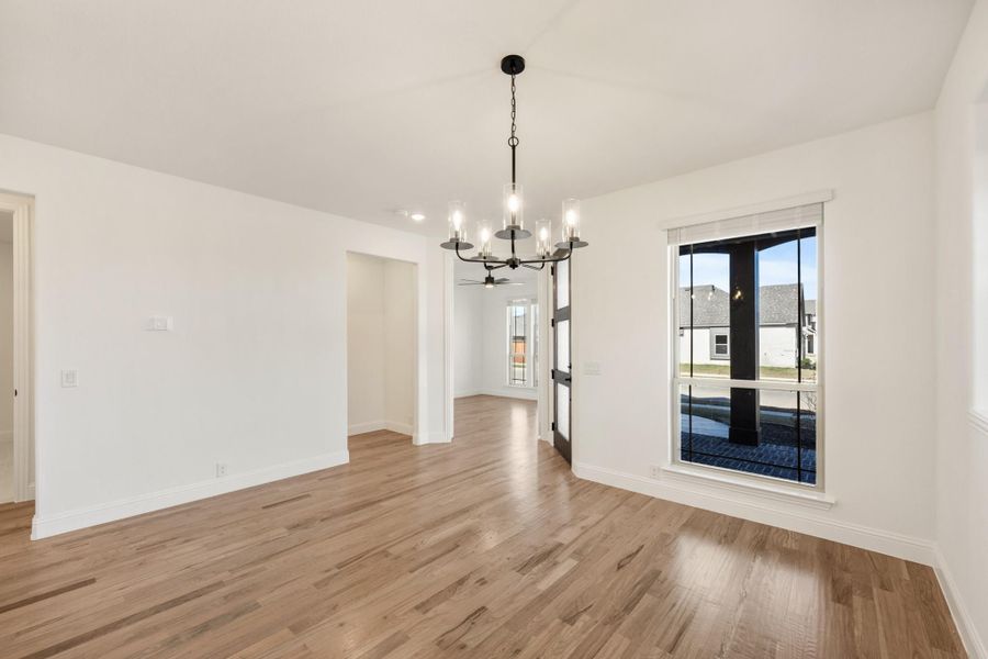 Empty dining room with hardwood floors, black chandelier, and large window with white trim