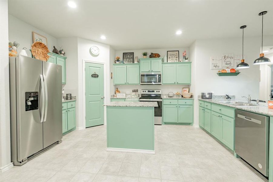 Kitchen featuring a center island, green cabinets, light stone counters, appliances with stainless steel finishes, and a sink