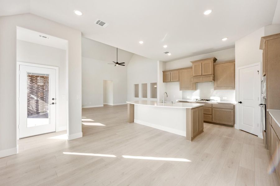 Open-concept kitchen with tan cabinets, center island, and light wood floors flowing into living area