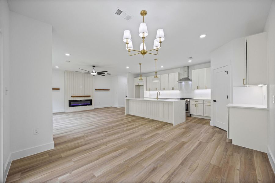 Spacious open-concept living area featuring wood-finish flooring throughout, a modern electric fireplace with shiplap accent wall, and a ceiling fan Spacious open-concept living area featuring wood-finish flooring throughout, a modern electric fireplace with shiplap accent wall, and a ceiling fan