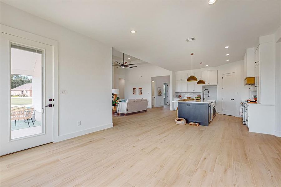 Kitchen with a center island with sink, light wood-type flooring, pendant lighting, white range, and white cabinetry