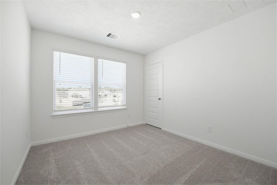 Secondary bedroom features plush carpet, neutral paint, lighting, large windows with privacy blinds, and a walk-in closet.