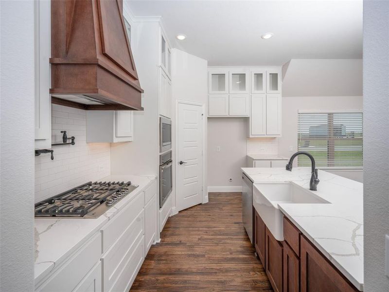Kitchen with tasteful backsplash, white cabinetry, light stone counters, dark wood-type flooring, and appliances with stainless steel finishes Kitchen with tasteful backsplash, white cabinetry, light stone counters, dark wood-type flooring, and appliances with stainless steel finishes